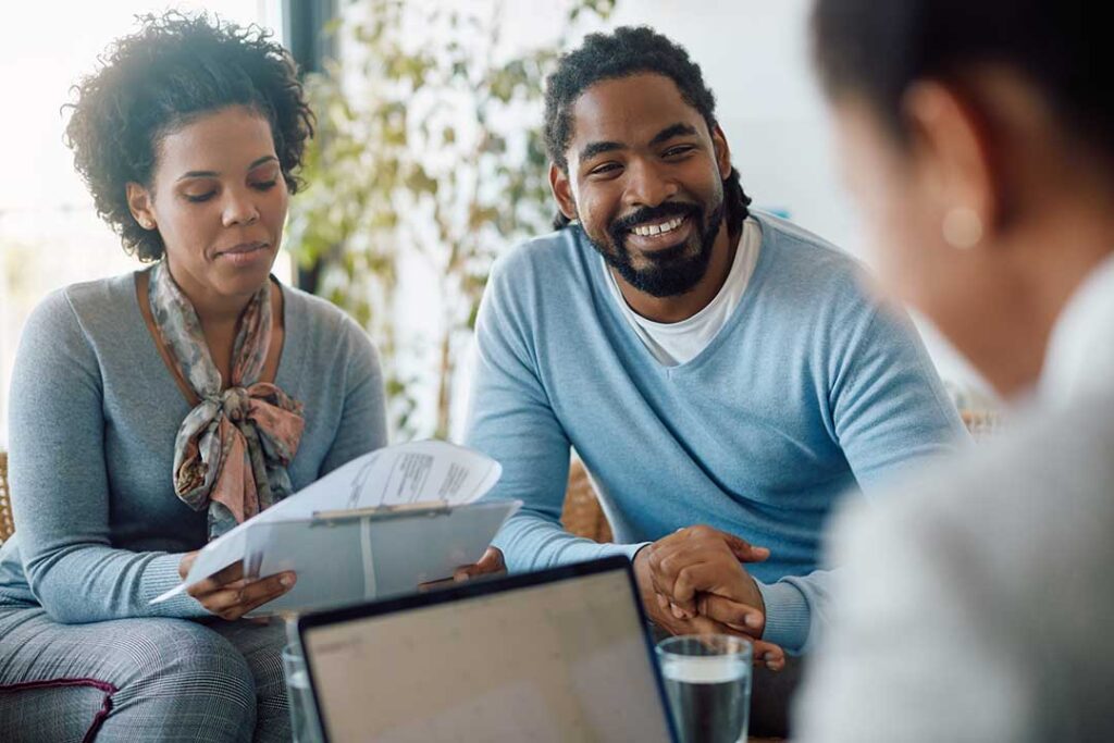 Parents review life insurance papers at a kitchen table while children play nearby.