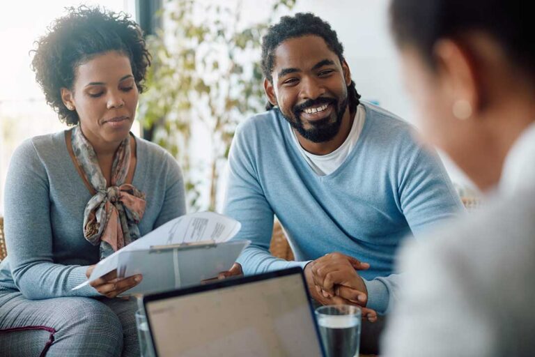 Parents review life insurance papers at a kitchen table while children play nearby.