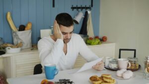A person reviews a life insurance denial letter beside medical records and a notebook at a kitchen table.